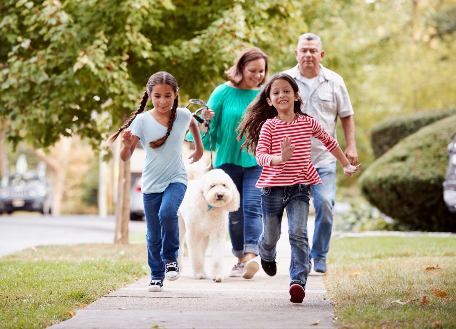Family walking their dog along a neighborhood sidewalk